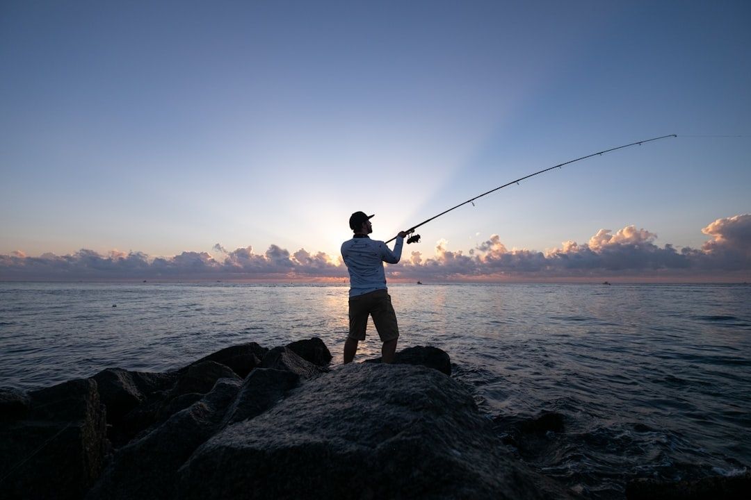 Sportsfisker kaster med fiskestang fra steiner ved kysten i vårsolen