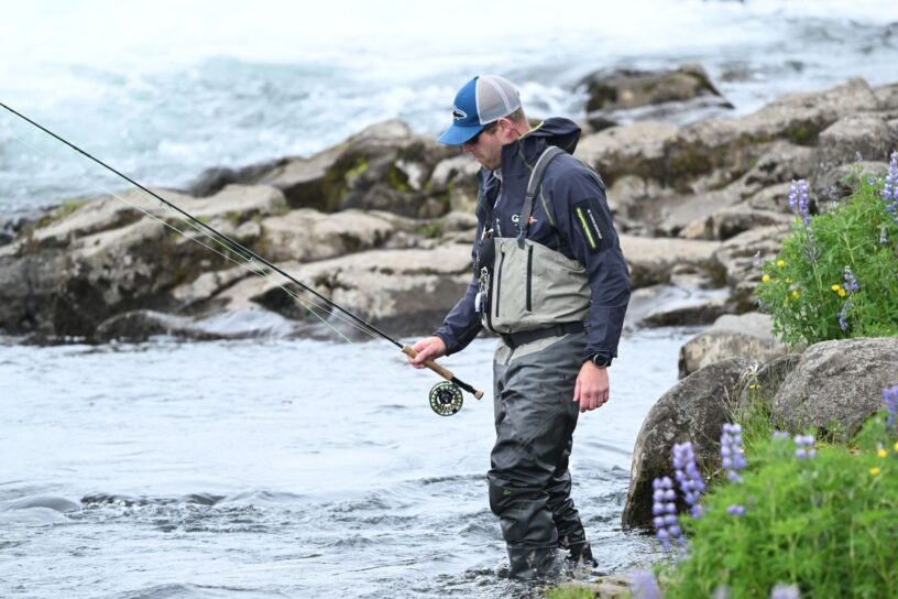 Fluefisker vader langs en steinete kyst med stang i hånden